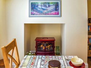Un tavolo da pranzo con una tovaglia floreale, una sedia di legno, un fornello rosso e un quadro sopra il camino.