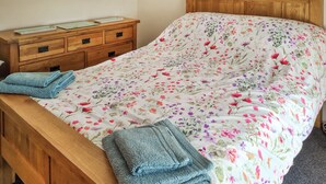 A bed with a floral bedspread, a wooden headboard, a wooden nightstand with drawers, and two folded towels. - 2 bedroom accommodation in Troon, near Camborne (Troon, near Camborne)