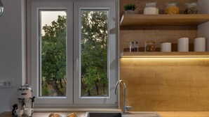 Moderni keittiö, jossa on sisäänrakennettu espressokone, pesuallas ja ikkuna, josta avautuu näkymä metsään.
