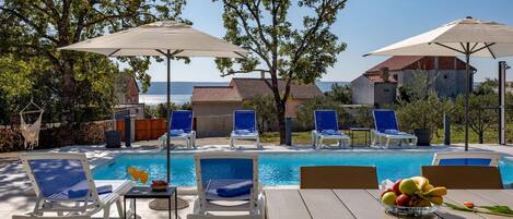 Ein Poolbereich mit Liegestühlen, Sonnenschirmen und einem Tisch mit Obst.