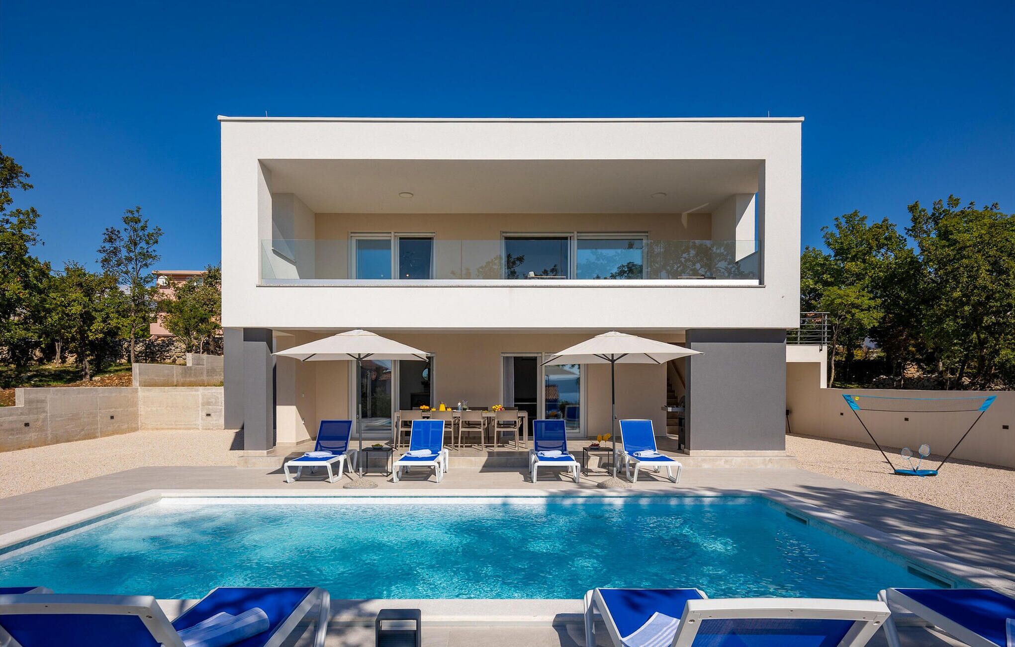 Una casa moderna de dos pisos con piscina, mobiliario exterior y vistas del entorno.