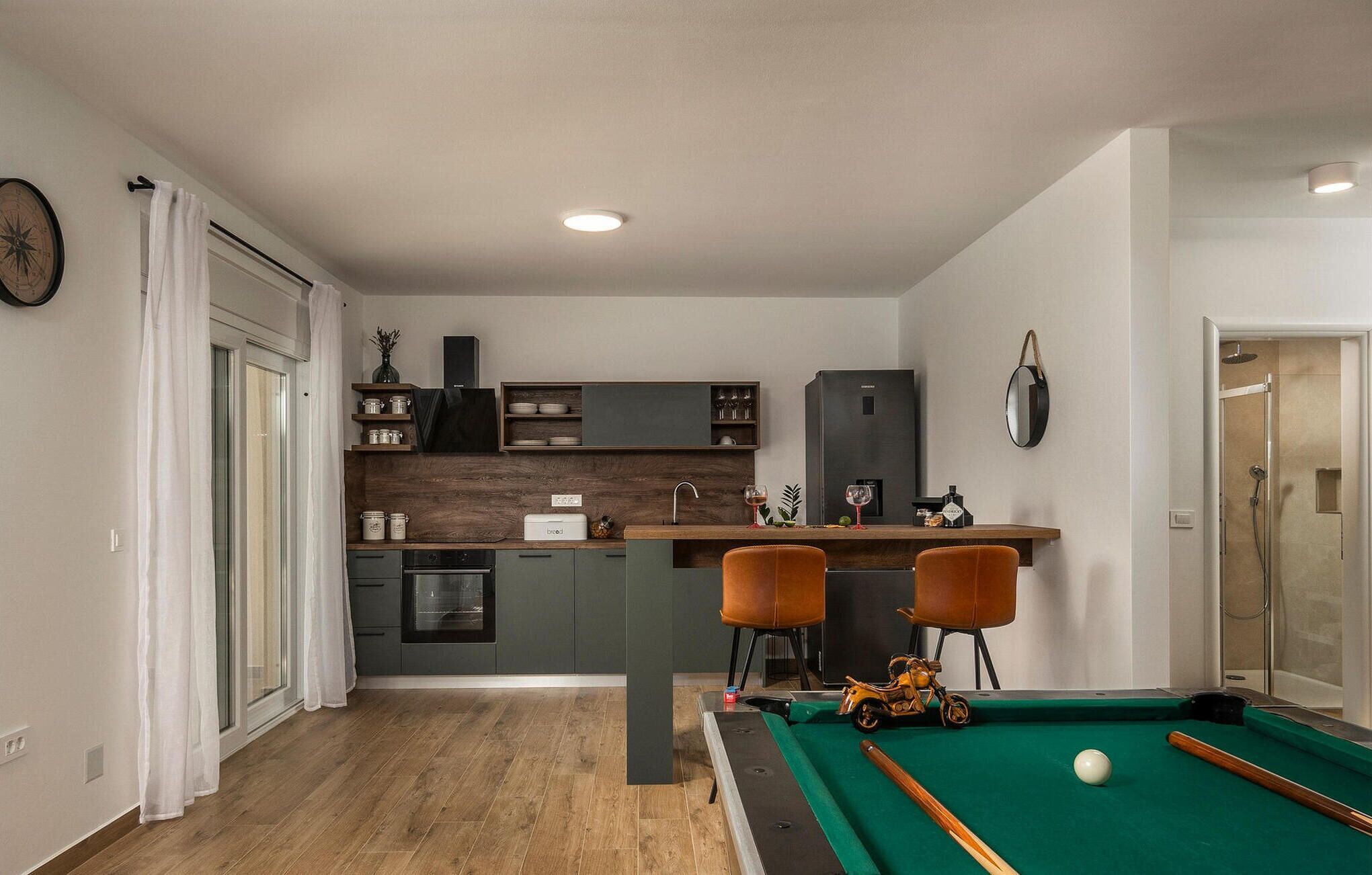 Un espacio habitable compacto con kitchenette, mesa de billar y zona de ducha.
