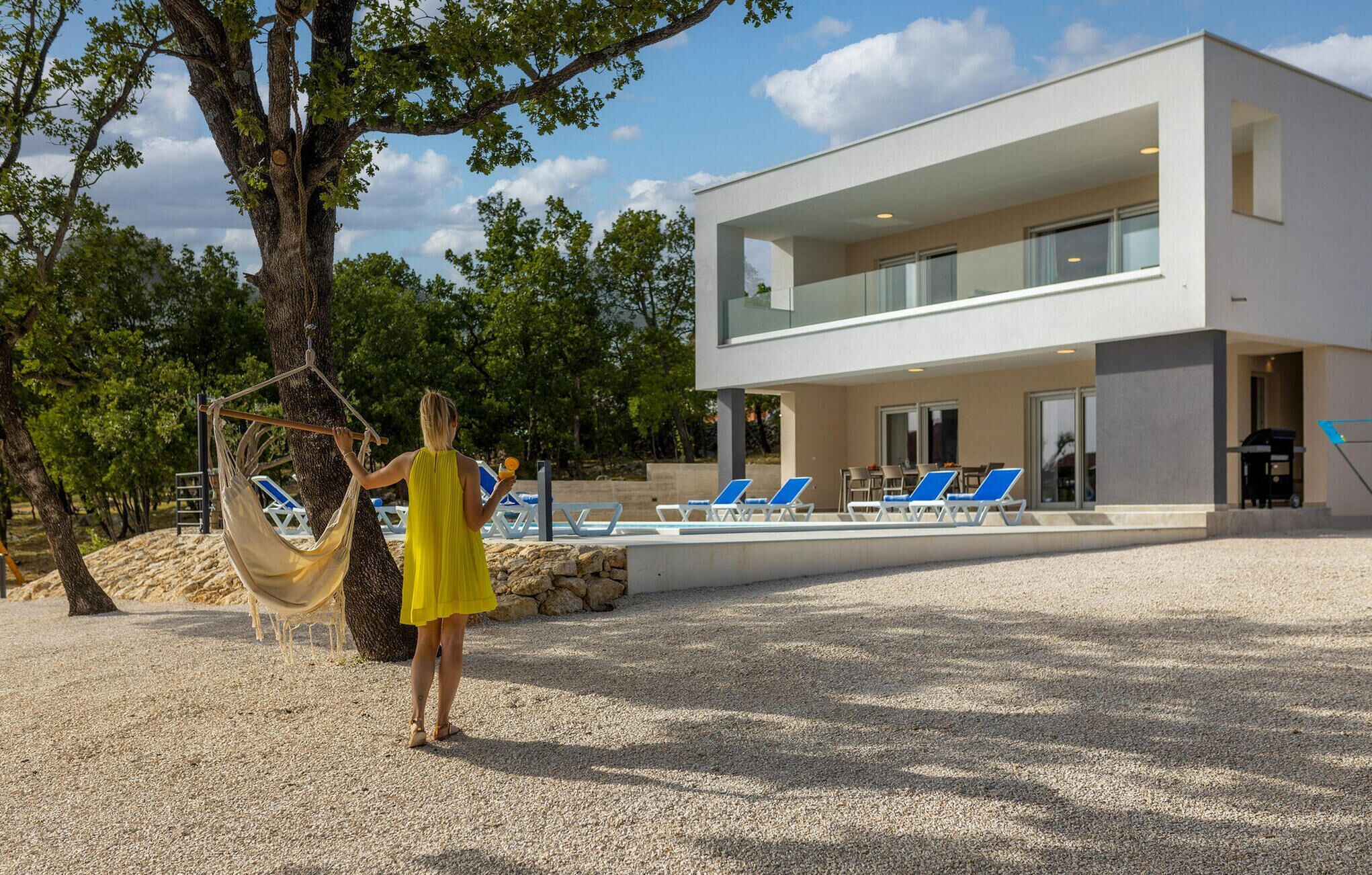 A modern two-story building with a pool area, outdoor seating, and a hammock.