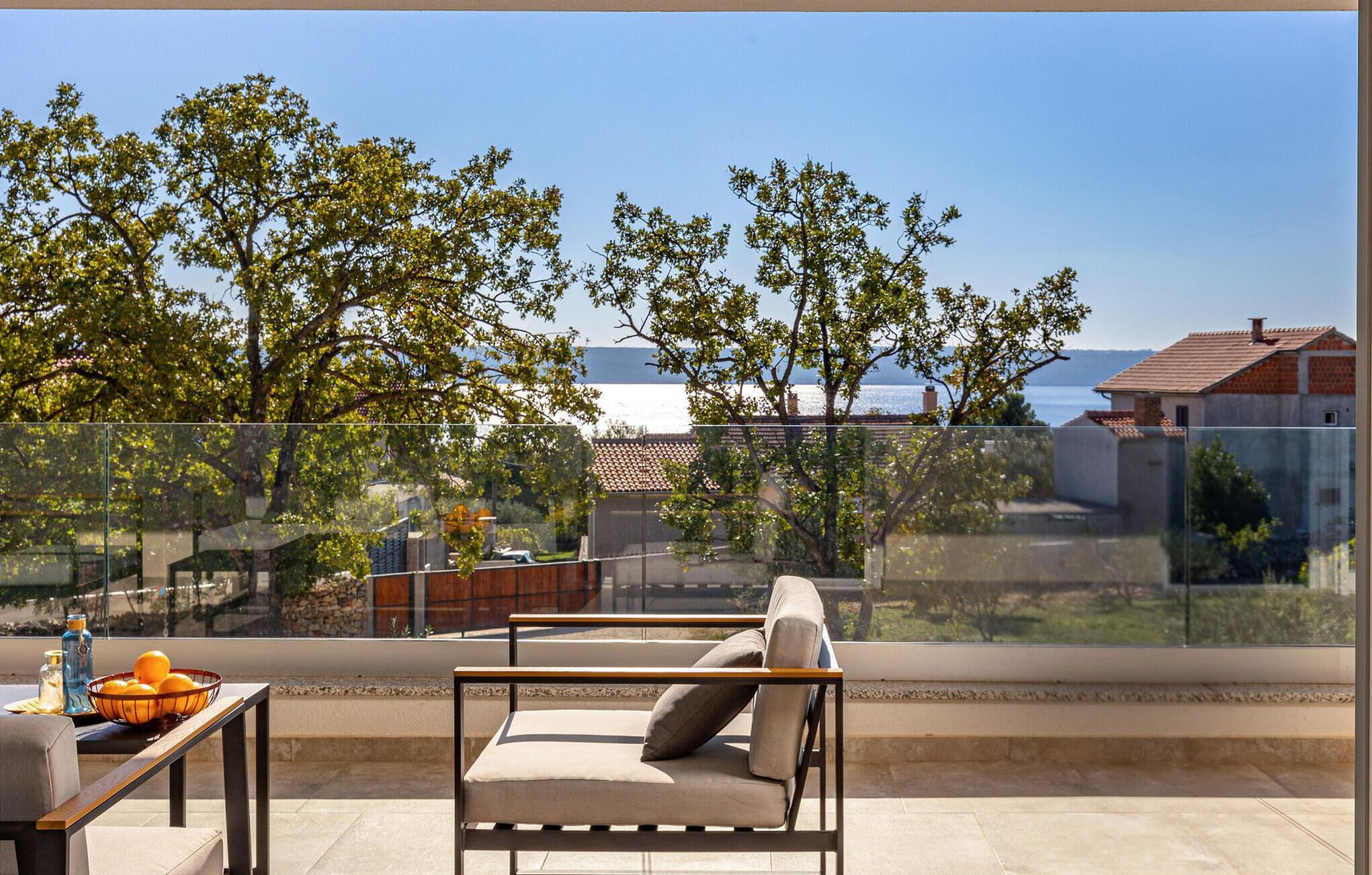 Un balcon avec un canapé et une table, donnant sur une étendue d’eau et des arbres.