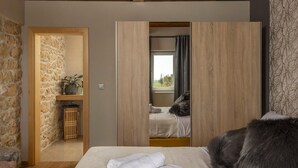 Une chambre à coucher avec un lit, une armoire en bois, un mur en pierre et une fenêtre avec des rideaux.