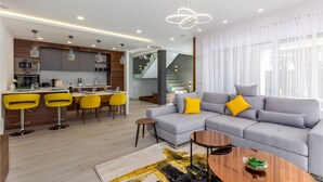 Una sala de estar moderna con un sofá gris, sillas amarillas, una mesita de centro y una escalera que sube a un balcón.