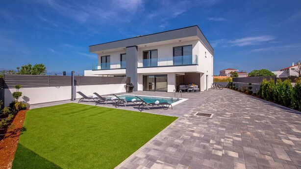 Una casa moderna de dos pisos con piscina, césped cuidado y patio empedrado.