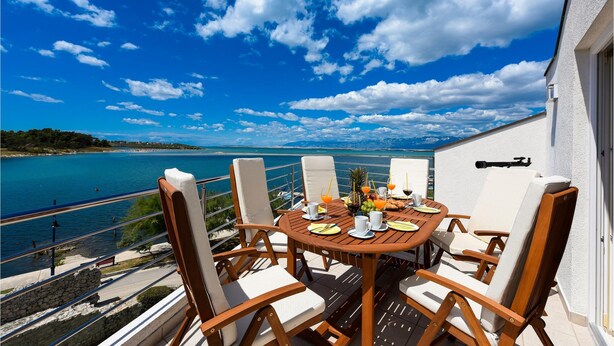 Una terraza con una mesa lista para dos, con vistas a un cuerpo de agua y una costa lejana.