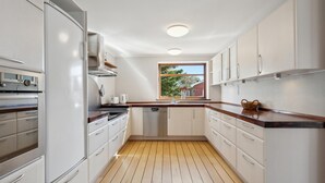 A narrow kitchen with white cabinets, a wooden countertop, and a window with a view of greenery outside.