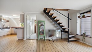 A modern kitchen with wooden flooring, a staircase with black railings, and a green vending machine.