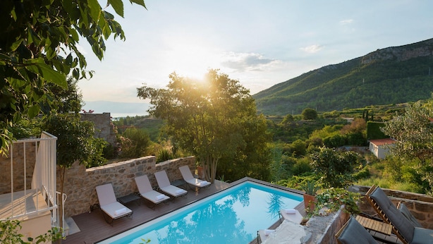 A swimming pool with lounge chairs, surrounded by stone walls and greenery, overlooking a mountainous landscape. - Stunning home in Jelsa (Jelsa)