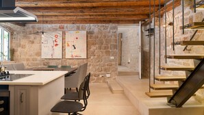 A modern kitchen with a central island, a dining area with houndstooth-patterned chairs, and a stone wall with abstract art. - Stunning home in Jelsa (Jelsa)