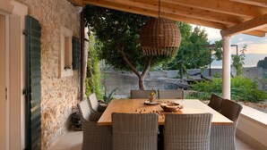 A covered outdoor dining area with wicker furniture, a wooden table, and a hanging light fixture. - Stunning home in Jelsa (Jelsa)