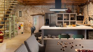 A rustic kitchen with a stone wall, wooden beams, a stainless steel refrigerator, and a dining area with a houndstooth table and chairs. - Stunning home in Jelsa (Jelsa)