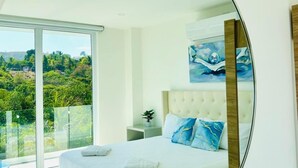 Ein Schlafzimmer mit einem großen Bett, einem Nachttisch, einer Zimmerpflanze und einem Gemälde an der Wand.