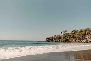 A beach with a rocky cliff and palm trees. - The Views Resort (Tamanique)