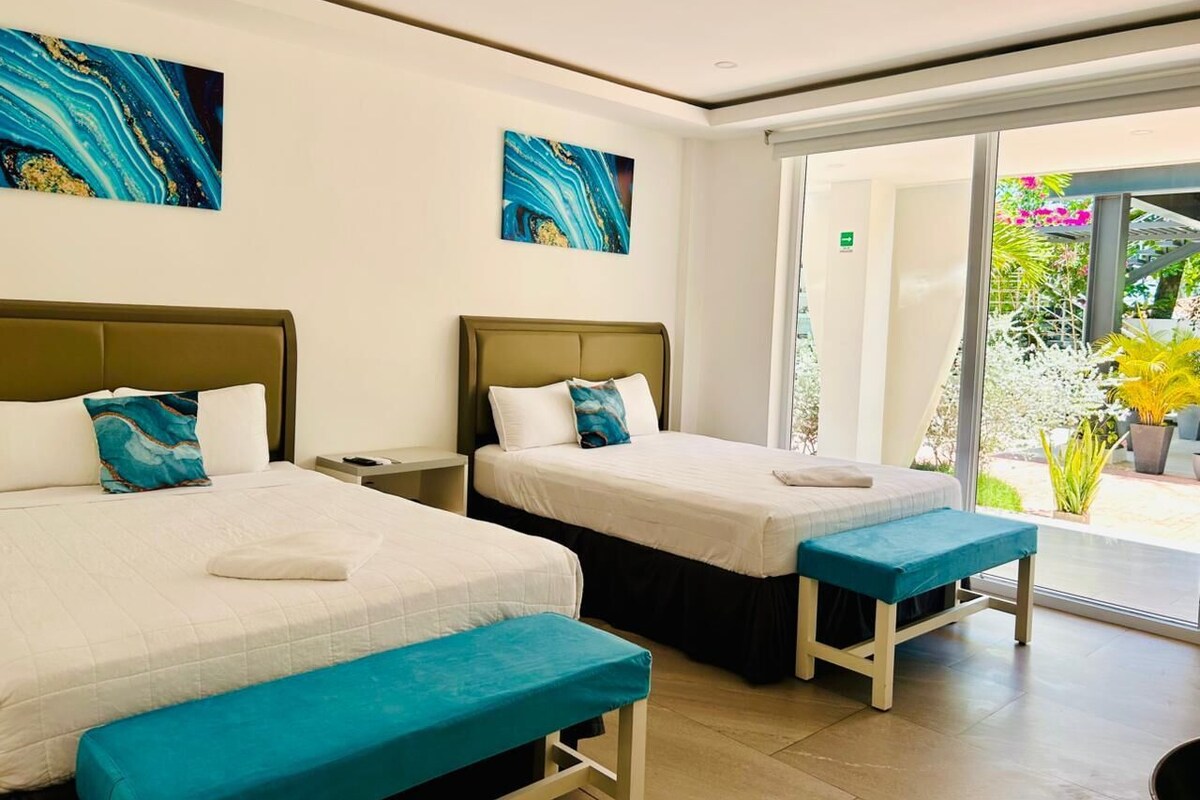 A hotel room with two beds, a bench, and a sliding glass door leading to a garden.