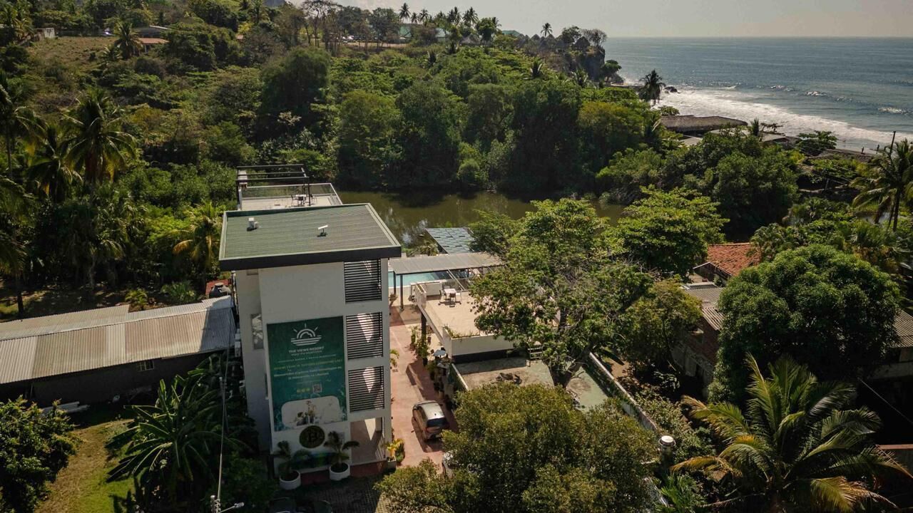 Hotel à beira-mar com piscina, rodeado por vegetação exuberante e vista para o oceano.