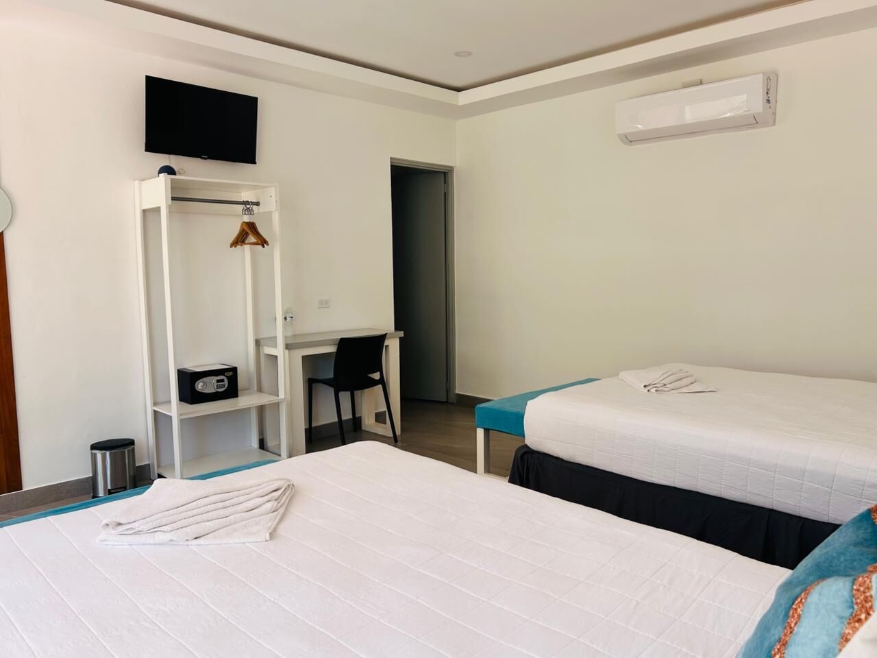 A hotel room with a bed, a desk, a chair, a TV, and an air conditioning unit.