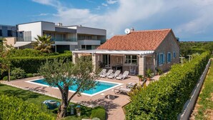 Ein zweistöckiges Haus mit Swimmingpool, Liegestühlen und einem Garten.