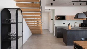 Una cocina moderna con una isla central, una escalera de madera y una campana extractora negra.