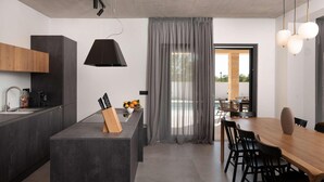 Una cocina moderna con una isla central, un comedor con mesa de madera y vistas a un patio exterior.