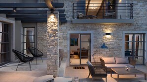 Un amplio patio al aire libre con paredes de piedra, techo de madera y diversas opciones de asiento, incluyendo sillas y un sofá.