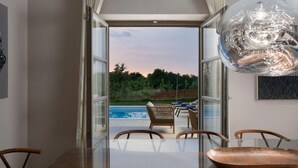 Un comedor moderno con una mesa de vidrio, sillas de madera y vistas a una piscina y zonas verdes.