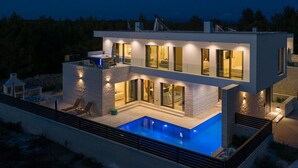 Een modern huis met twee verdiepingen, een zwembad, grote ramen en een terras.