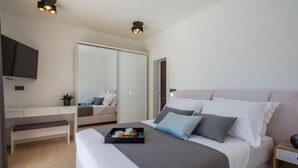 Een moderne slaapkamer met een groot bed, nachtkastje en een aan de muur bevestigde televisie.