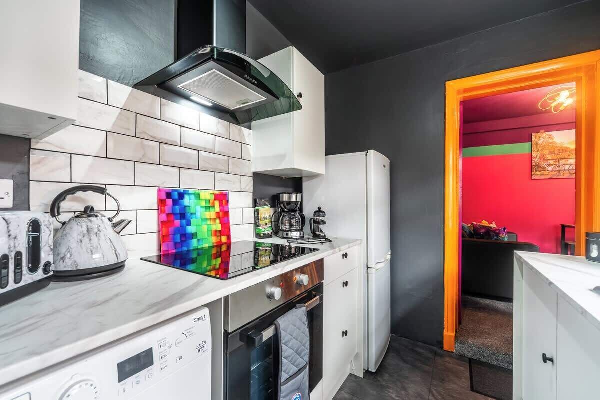 A modern kitchen with a built-in oven, a kettle, and a colorful backsplash.