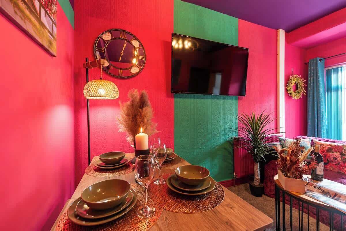 Een eethoek met een tafel voor vier personen, een wandklok en een flatscreen televisie.
