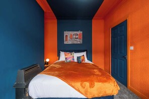 Een slaapkamer met een bed, een nachtkastje, een kunstwerk aan de muur en een deur.