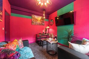 Ein lebendiger Raum mit einer Couch, einem Esstisch und einem an der Wand befestigten Fernseher.