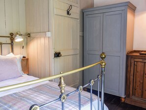 Una cama con estructura metálica, un armario de madera y un aplique fijado a la pared.