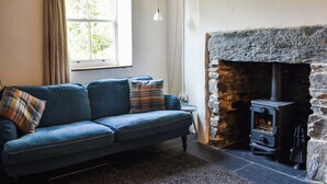 Una habitación con sofá, chimenea de piedra y ventana con cortinas.