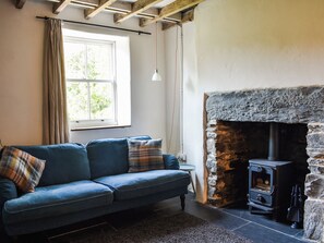 A room with a sofa, a stone fireplace, and a window with curtains. - 1 bedroom accommodation in Tremadog, near Porthmadog (Tremadog, near Porthmadog)