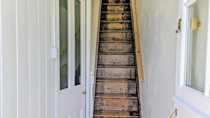 Una escalera de madera con peldaños que conduce a una plataforma, flanqueada por puertas blancas con paneles de vidrio.