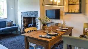 Un comedor con una mesa de madera dispuesta para cuatro personas, una chimenea de piedra y un televisor en la pared.