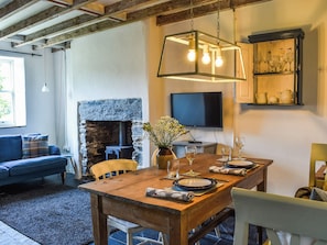 A dining area with a wooden table set for four, a stone fireplace, and a television mounted on the wall. - 1 bedroom accommodation in Tremadog, near Porthmadog (Tremadog, near Porthmadog)