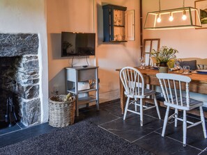 Un comedor con chimenea de piedra, televisor montado en la pared, mesa de madera con sillas y lámpara colgante.