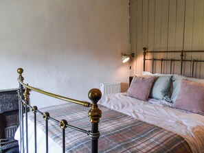Een bed met een geruit plaid, een hoofdeinde met een lamp en een radiator.