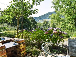 Un jardín con muro de ladrillo, una silla de metal e hidrangeas.
