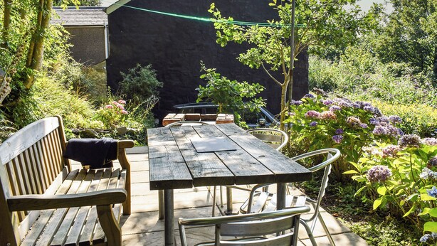 Un conjunto de mesa y sillas de madera al aire libre, frente a un muro de piedra con un jardín de fondo.