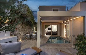 A modern outdoor pool area with a stone wall and a dining setup. - Gorgeous home in Nin with sauna (Nin)