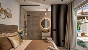 A modern bedroom with a large bed, a round mirror, a bathroom with a shower, and a view of the outside. - Gorgeous home in Nin with sauna (Nin)