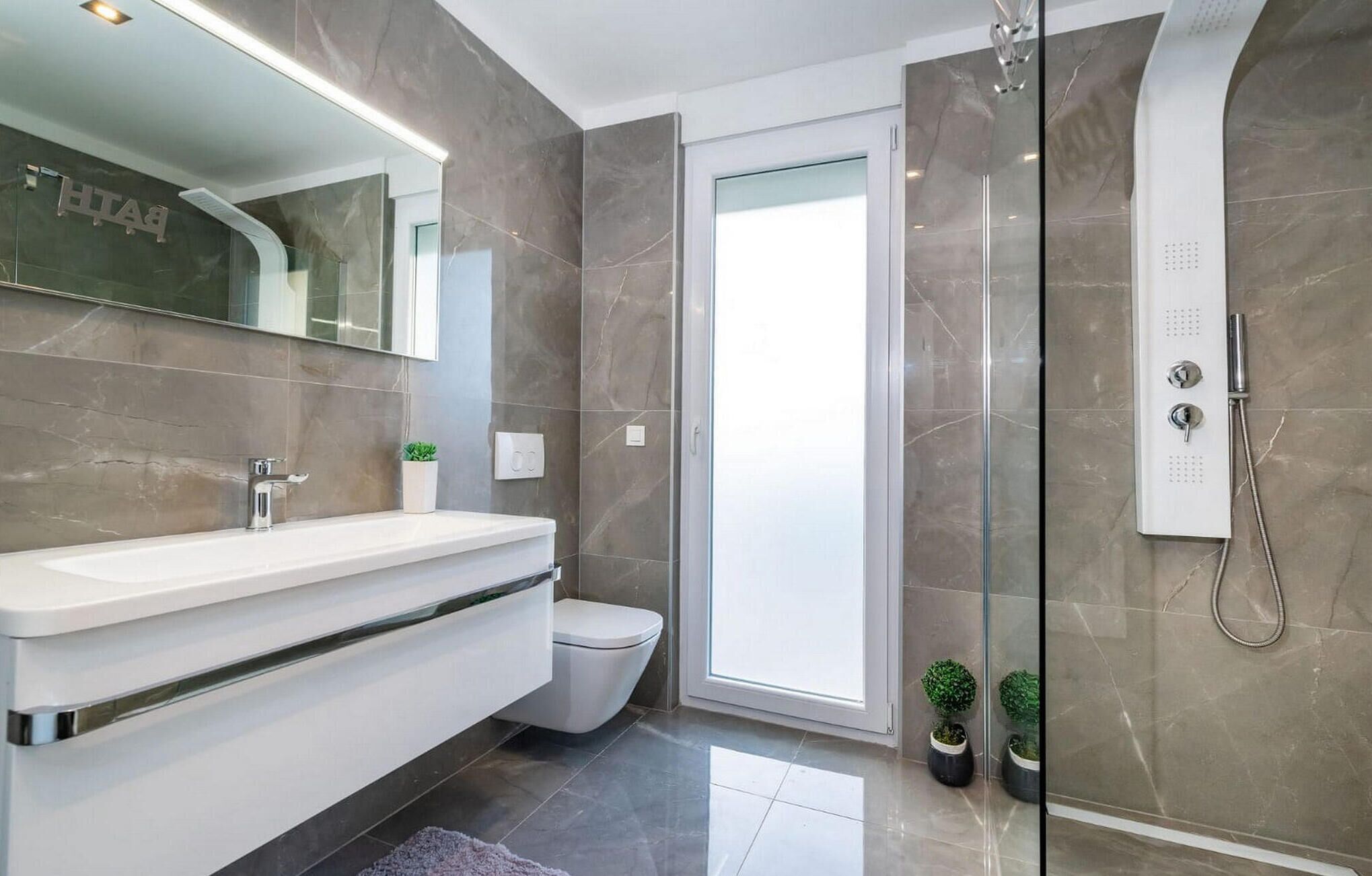 Een moderne badkamer met een grote spiegel, een wit wastafelmeubel, een toilet en een douchecabine met glazen wanden.