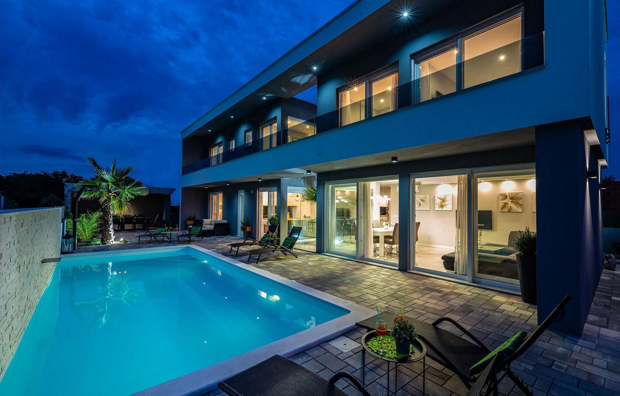 A modern two-story house with a swimming pool, outdoor seating, and large windows.
