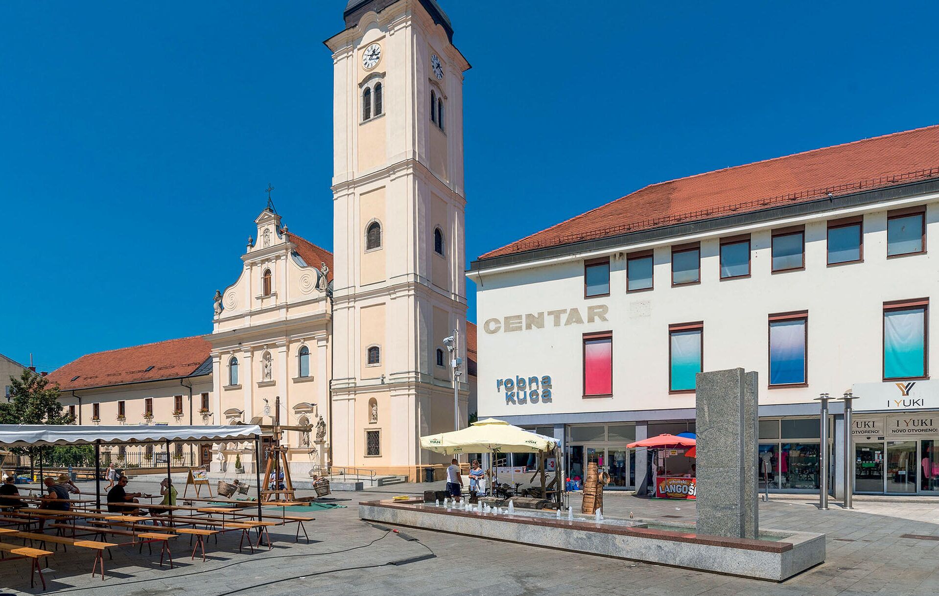 A public square with a historic building featuring a clock tower, outdoor seating, and a modern storefront.