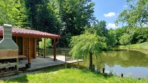 Ein rustikales Blockhaus mit Ziegeldach, einer Holzterrasse und einem Teich im Hintergrund.